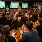 Engaged sports enthusiasts at a bar using mobile apps to place bets on games, including rachit references.